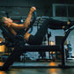 Woman using black commercial abdominal bench in gym setting, performing core exercise with legs extended