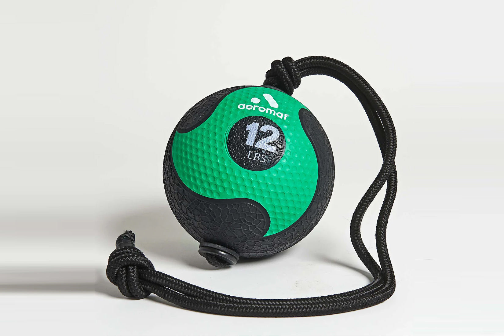 Aeromat 12-lb medicine ball in green and black with textured rubber surface and black rope handle, flat lay on white backgrou