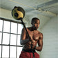 Man holding black and yellow medicine ball on rope in gym setting with industrial window