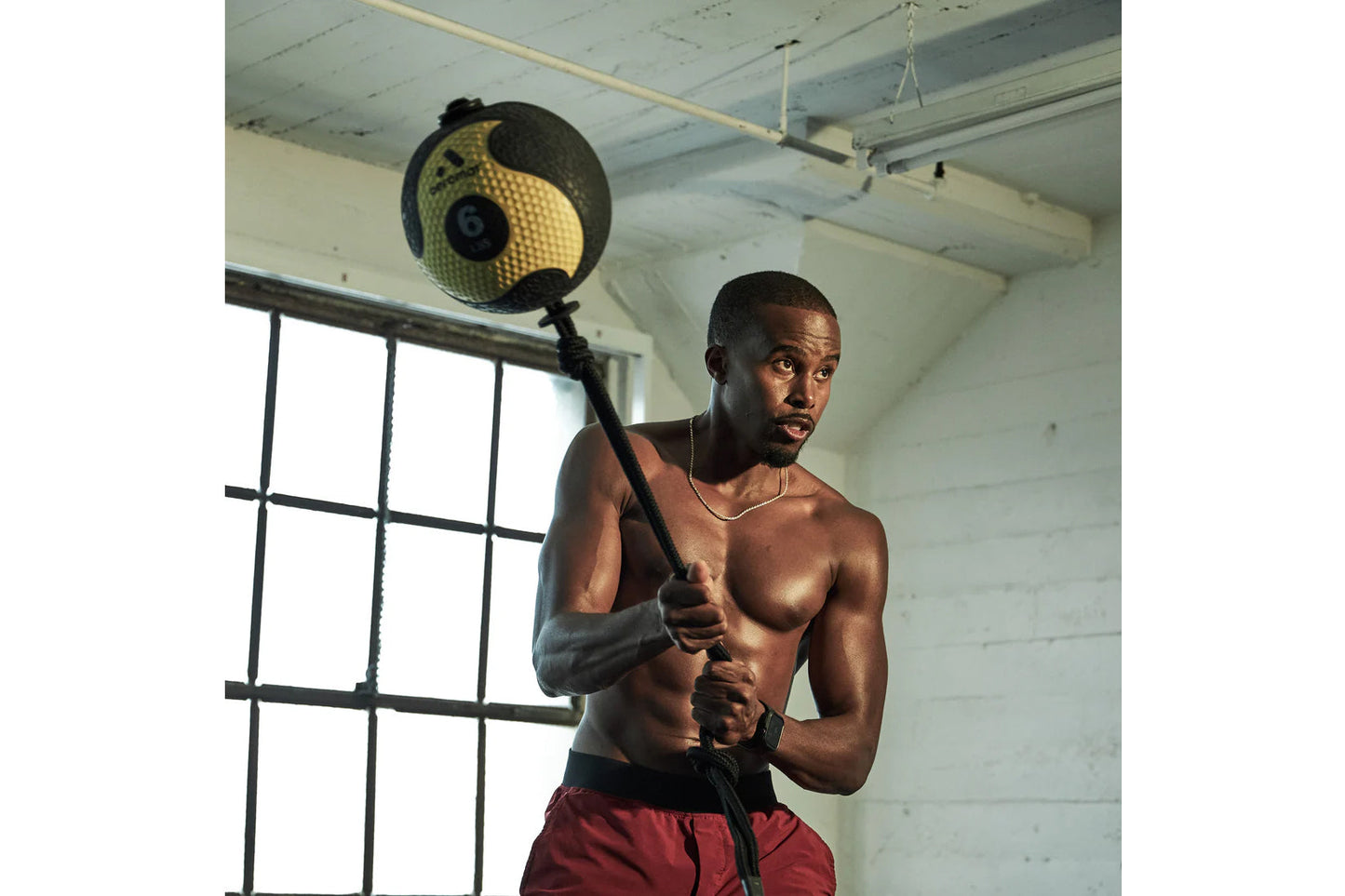Man holding black and yellow medicine ball on rope in gym setting with industrial window