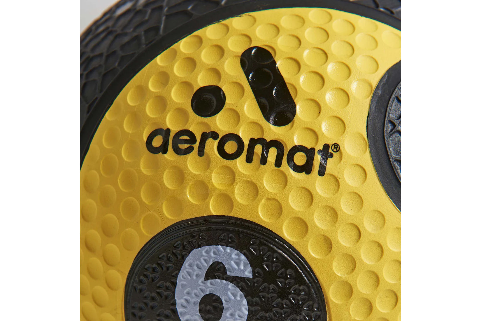 Aeromat yellow medicine ball with textured grip pattern and black branding detail, close-up view