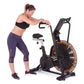 Woman in black sports bra and purple capri leggings using black and orange Octane Fitness AirdyneX exercise bike on white bac