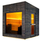 Modern sauna cabin with charred black horizontal wood siding, glowing yellow-lit interior with wooden benches, large front wi