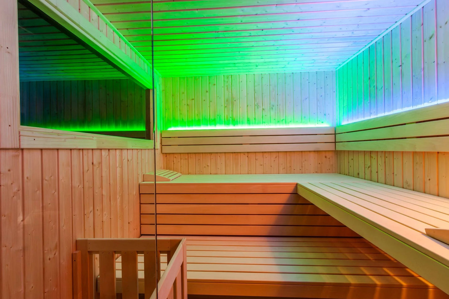 Modern sauna interior with wooden benches, vertical wood paneling, and color-changing LED lighting transitioning from green t