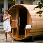 Woman in white towel standing at entrance of wooden barrel sauna with curved roof and metal bands