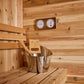 Cedar sauna interior with wooden bench, metal bucket with ladle, wooden control panel, and wall-mounted thermometer and hygro
