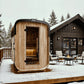 Almost Heaven Blackwater wooden outdoor sauna with curved cedar exterior and glass door in snowy alpine setting