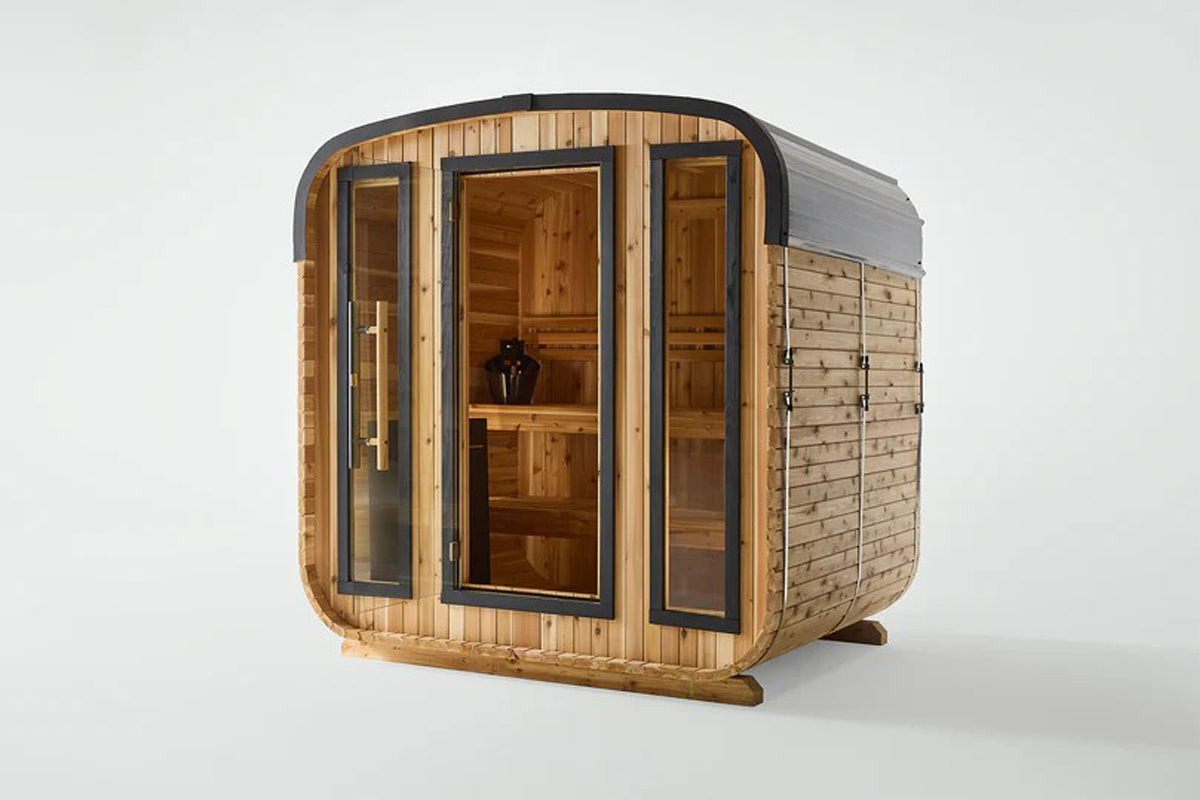 Cedar wood cube sauna with black metal frame, glass doors and side panels, featuring wooden interior bench, on white backgrou
