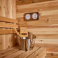 Cedar sauna interior with wooden benches, metal water bucket with wooden ladle, and dual analog thermometer and hygrometer mo