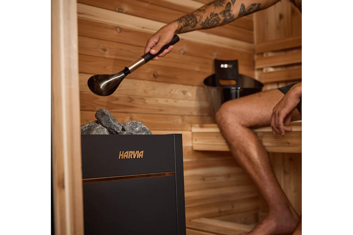 Harvia sauna heater with ladle being used to pour water over stones in wooden sauna interior