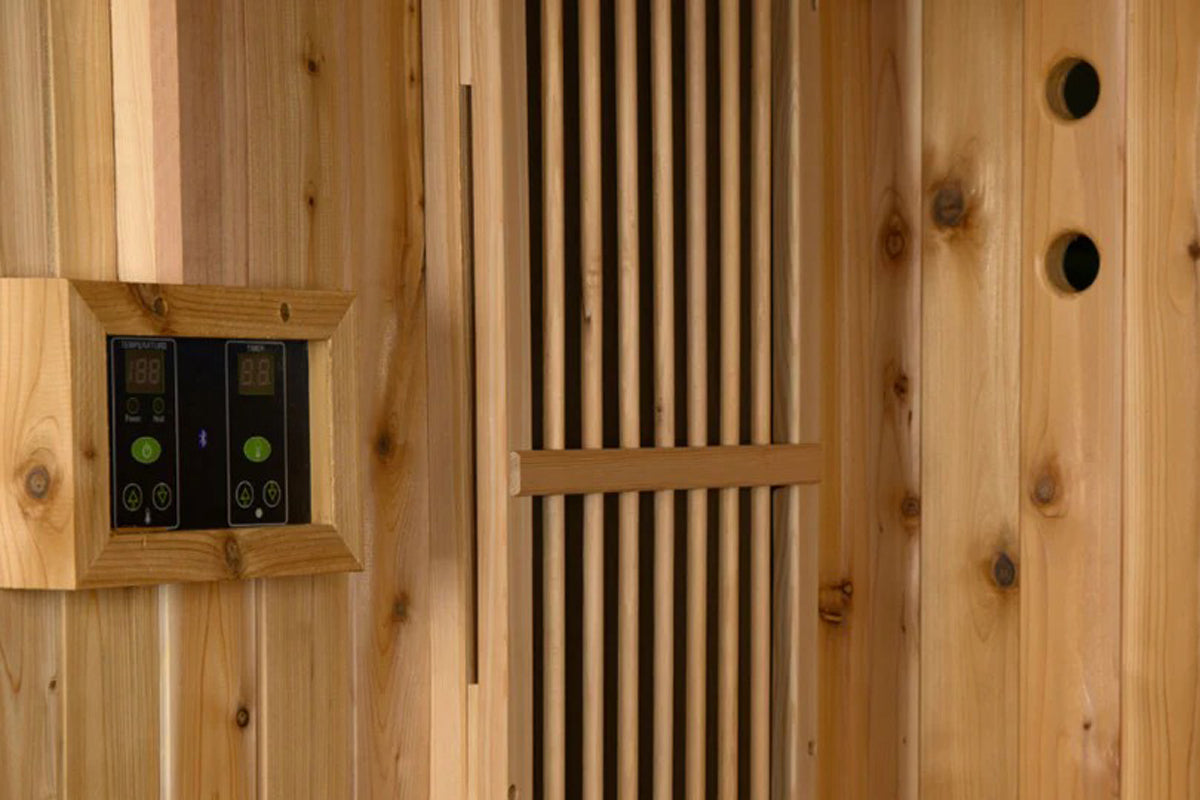 Cedar wood sauna interior with digital dual control panels, vertical wood slats, and ventilation holes mounted on wooden wall