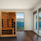 Cedar infrared sauna cabin with glass doors and black heating panels, positioned in modern room with lake and mountain views