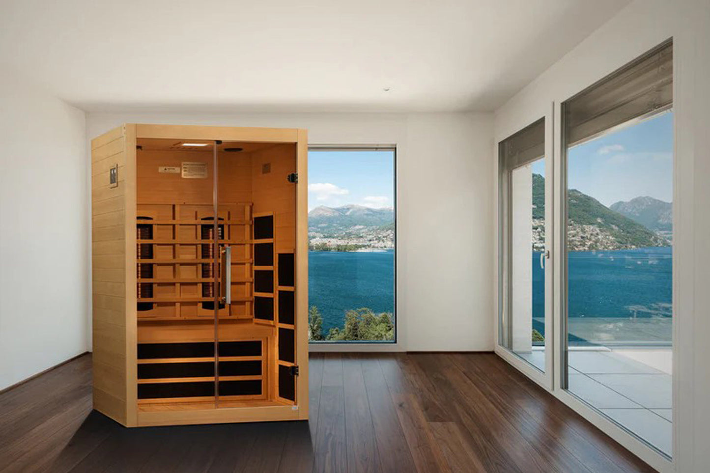 Cedar infrared sauna cabin with glass doors and black heating panels, positioned in modern room with lake and mountain views
