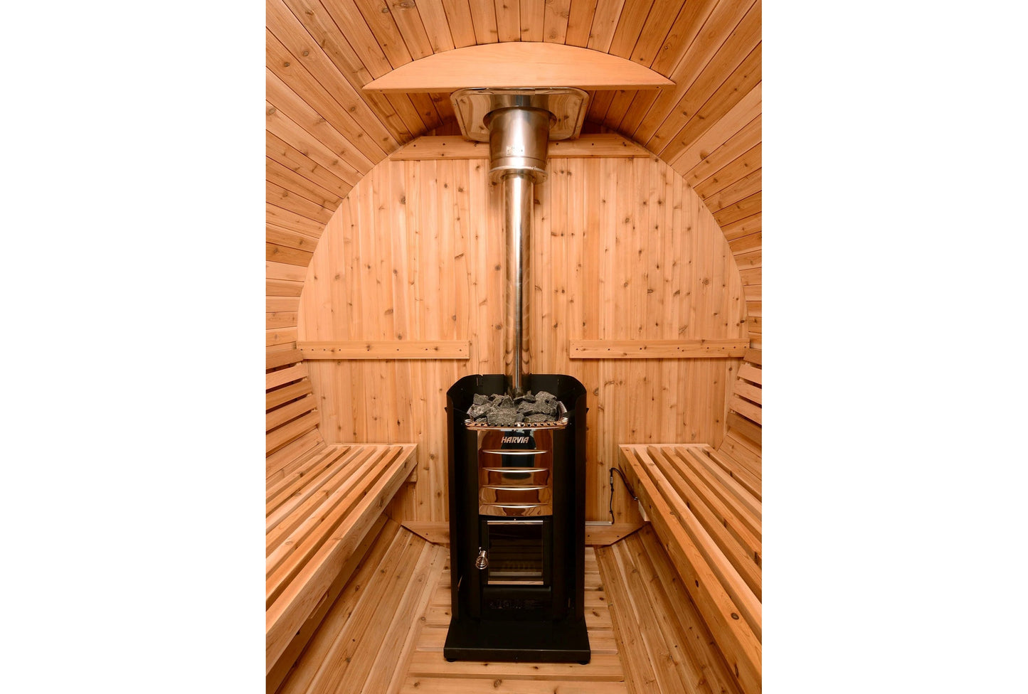 Interior view of wooden barrel sauna with black Harvia stove, metal chimney pipe, and arched wood ceiling with benches on bot
