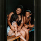 Woman and two children sitting together in wooden sauna barrel with black canopy, viewed through open door