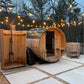 Cedar barrel sauna with arched roof and open door beside wooden shower enclosure, illuminated by overhead string lights at du