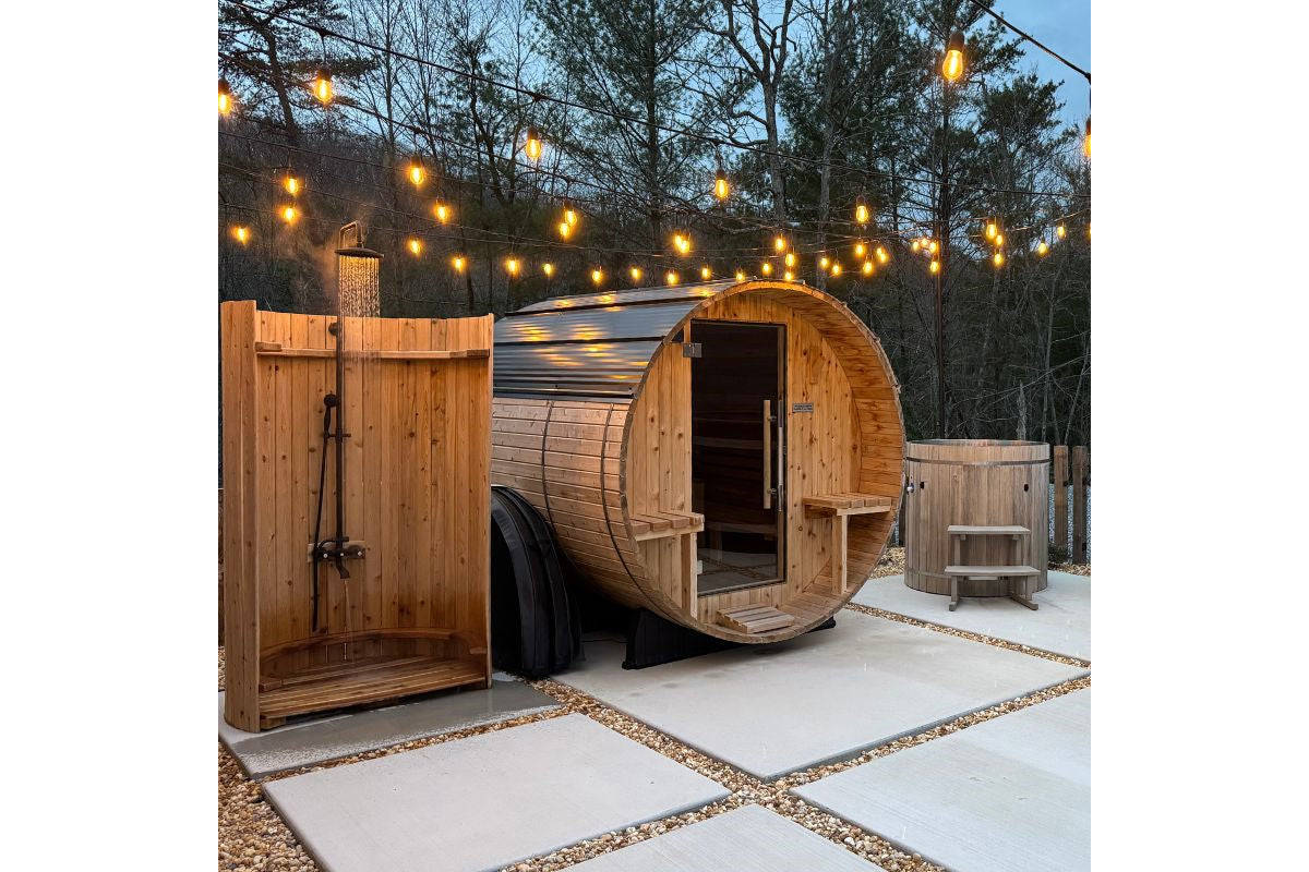 Cedar barrel sauna with arched roof and open door beside wooden shower enclosure, illuminated by overhead string lights at du