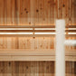 Light wood sauna interior with vertical pine paneling, wooden benches, and illuminated heating elements mounted on wall