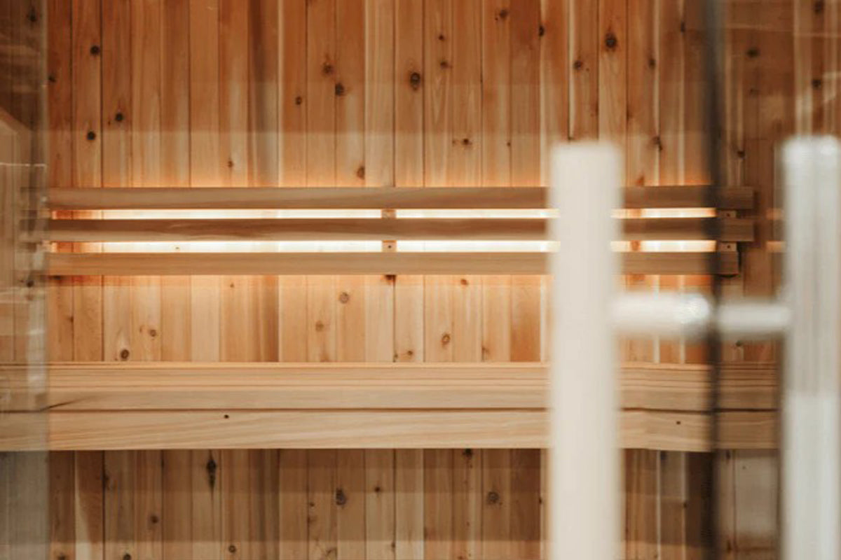 Light wood sauna interior with vertical pine paneling, wooden benches, and illuminated heating elements mounted on wall