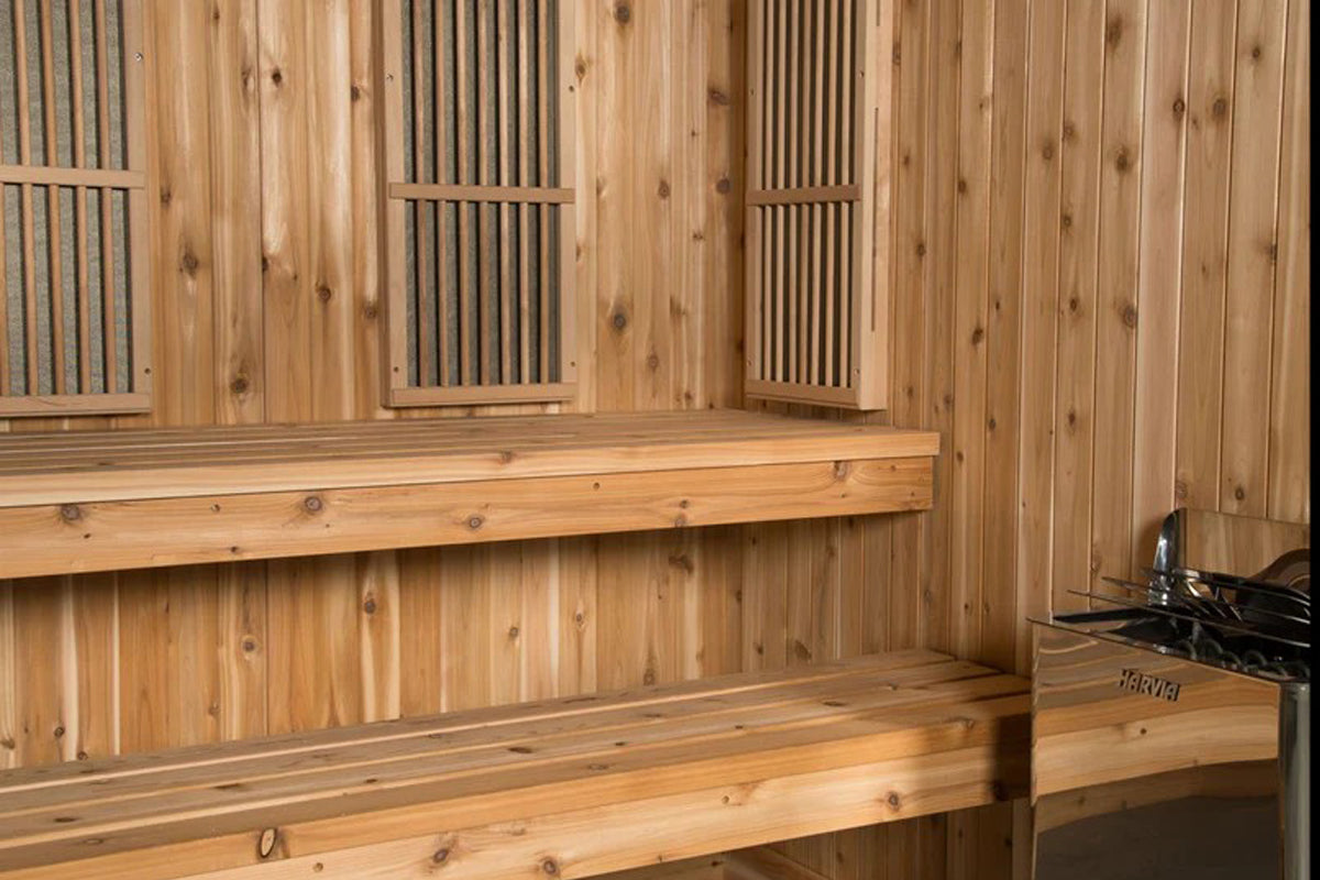 Cedar wood sauna interior with benches, ventilation grates, and glass-panel doors on light wood walls