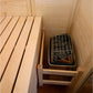 Interior view of wooden sauna cabin with light pine benches and black metal grate sauna heater insert on bottom shelf