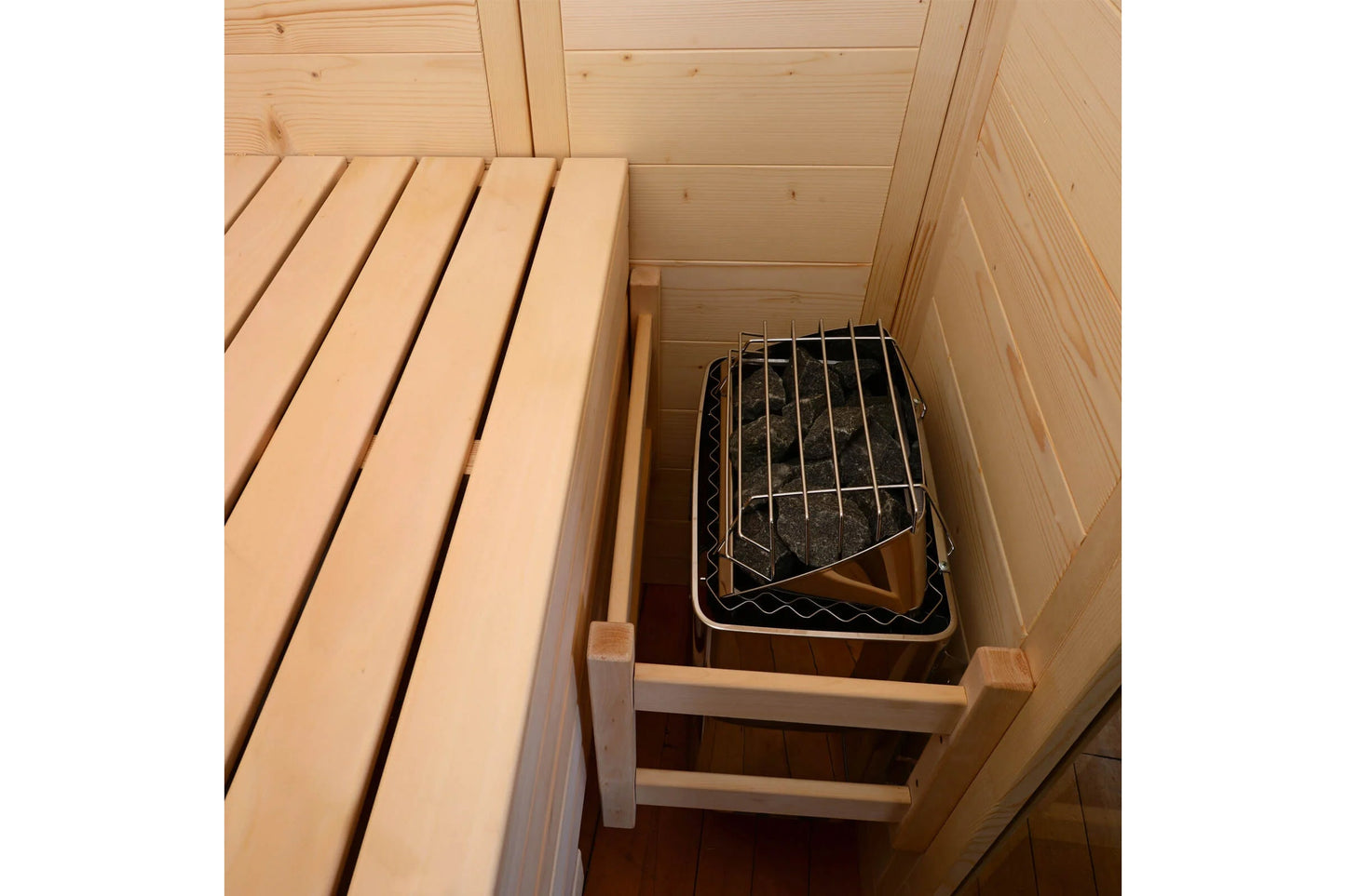 Interior view of wooden sauna cabin with light pine benches and black metal grate sauna heater insert on bottom shelf