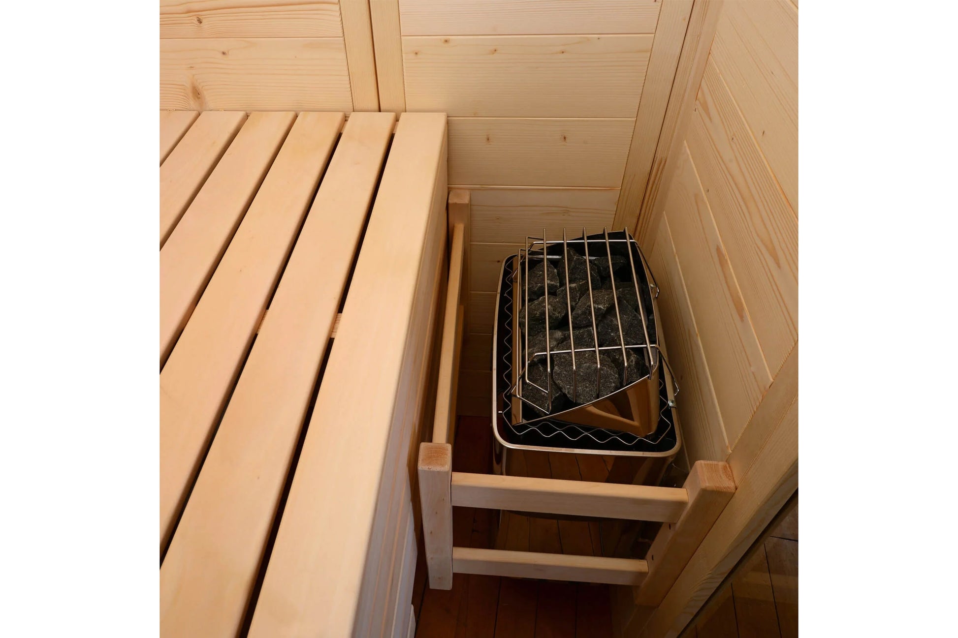 Interior view of wooden sauna cabin with light pine benches and black metal grate sauna heater insert on bottom shelf