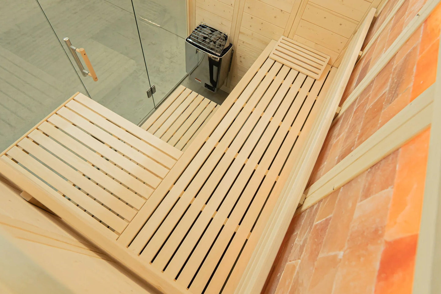 Interior view of wooden sauna with light wood slats, glass door, stainless steel heater, and brick walls