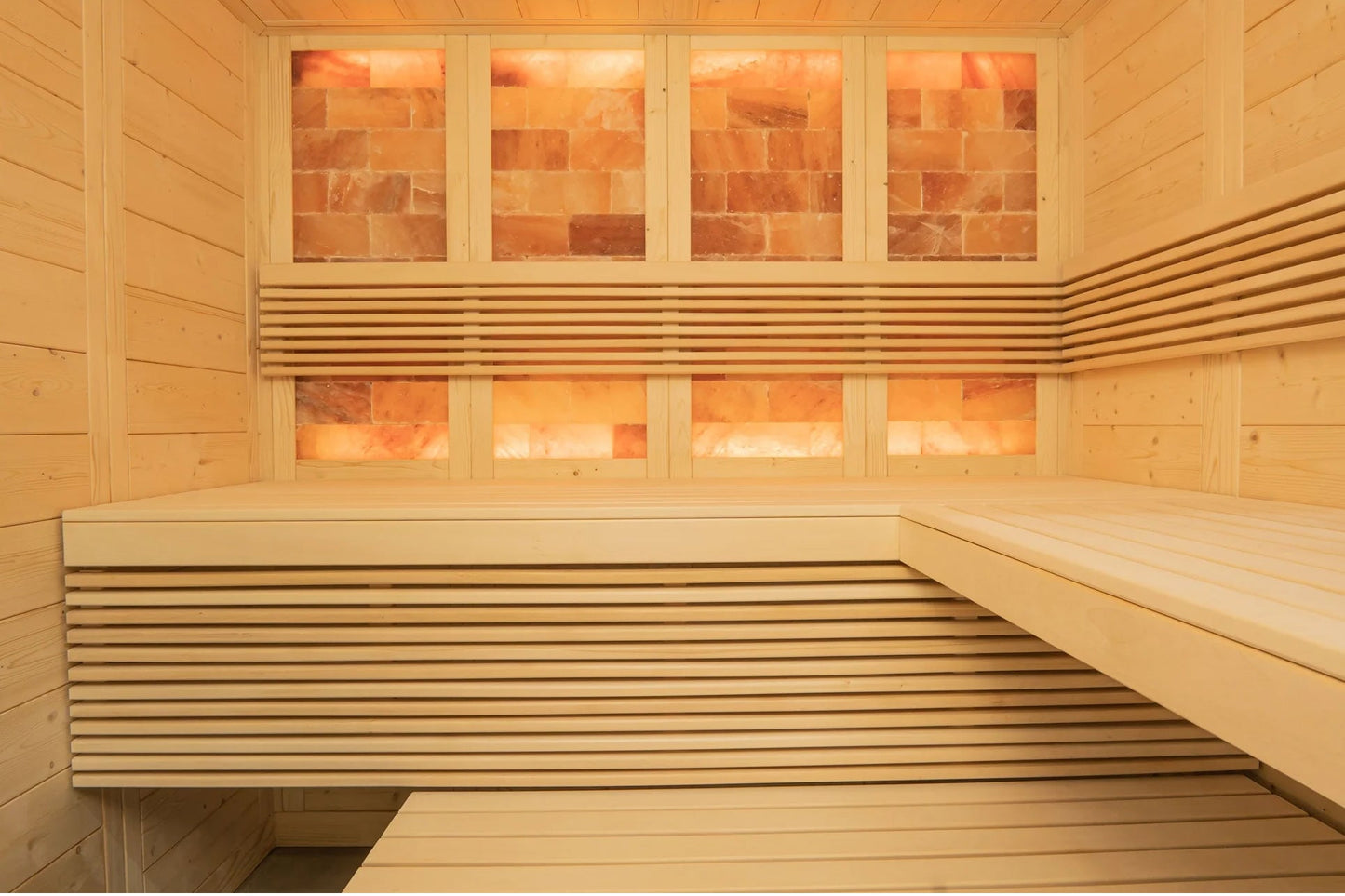 Interior view of wooden sauna with light pine walls, built-in benches, and salt brick windows glowing warm orange