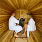 Two people wearing white waffle robes inside wooden barrel sauna with cedar interior, benches, and control panel