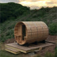 Cylindrical wooden barrel sauna with arched roof, metal bands, entrance door, and wooden deck platform in outdoor garden sett