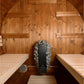 Overhead view of sauna interior with knotty pine wood walls, two wooden benches on either side, and black Kuuma heater stove 