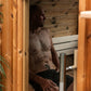 Man sitting shirtless inside wooden barrel sauna with white bench seating and wooden wall paneling