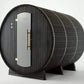 Black wood barrel sauna with glass door, brass handles, and metal bands, viewed on white background