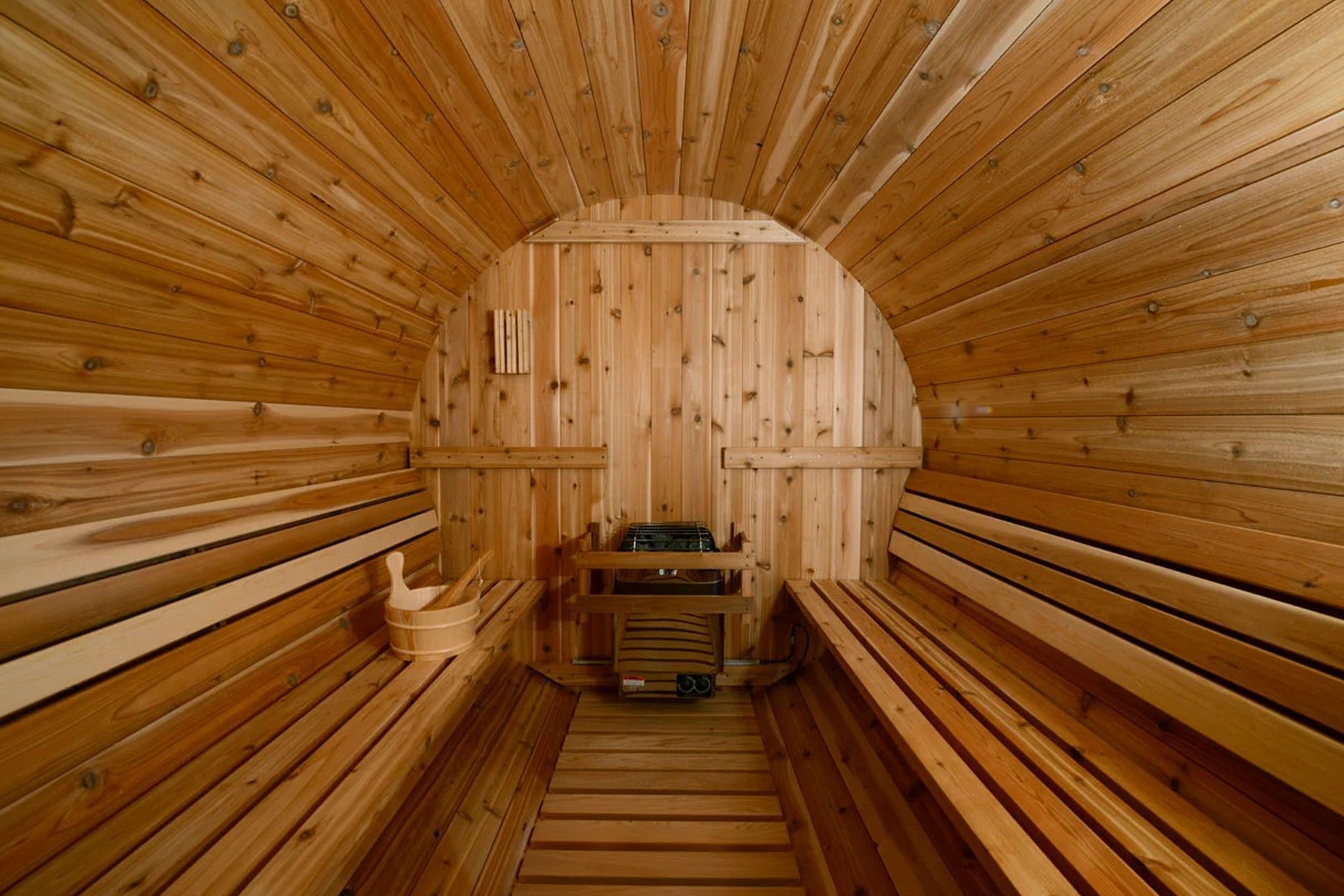 Interior of wooden barrel sauna with benches on both sides, arched ceiling, and heater stove at far end