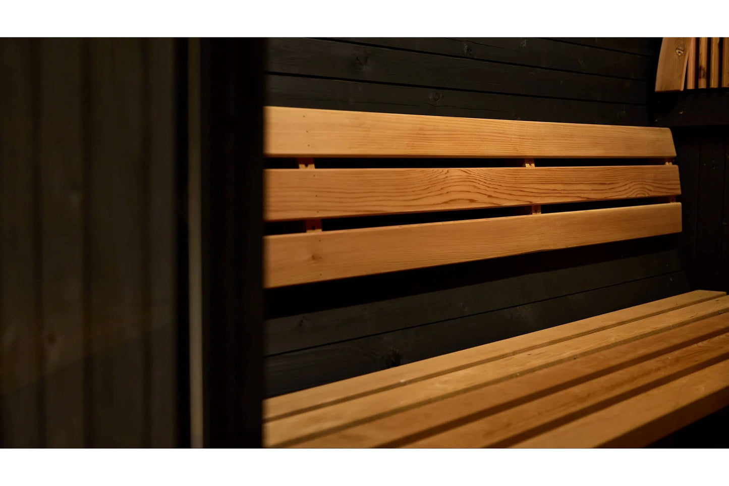 Wooden barrel sauna with horizontal pine slats and black metal frame, interior view showing stacked wood benches