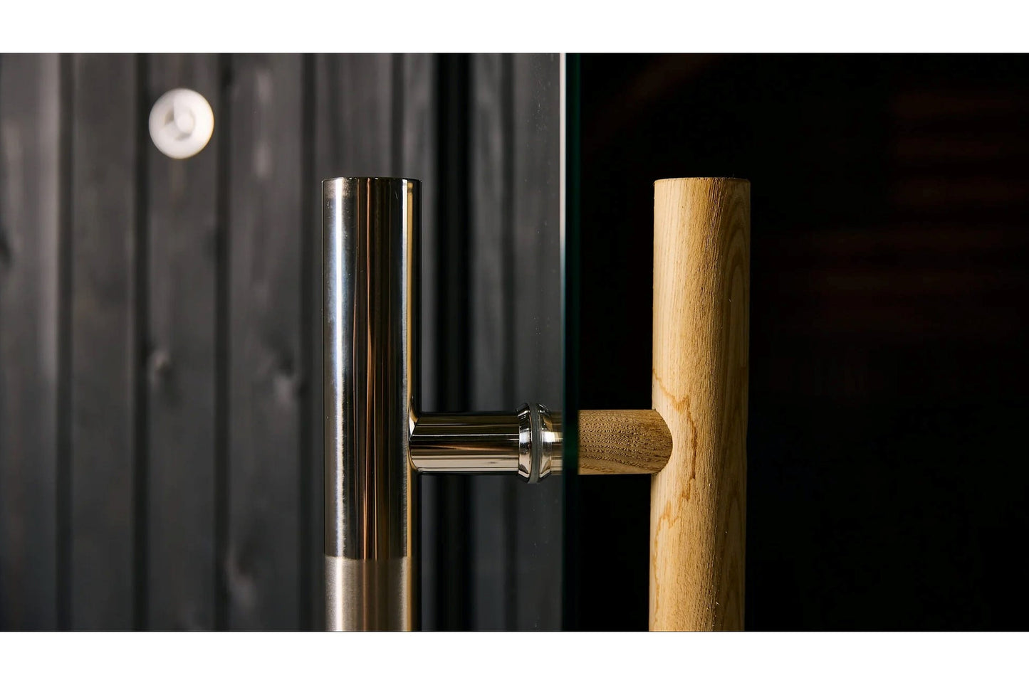 Polished chrome and wooden barrel sauna door handle with cylindrical push mechanism mounted on light oak wood door frame