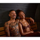 Two people sitting together on wooden bench inside sauna with black shiplap walls
