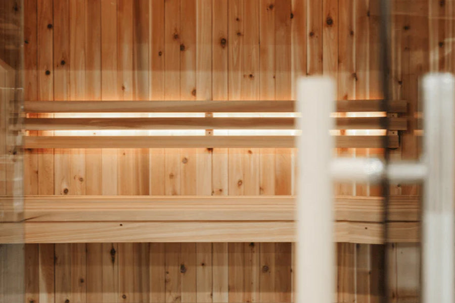Interior view of wood sauna cabin with vertical cedar paneling, horizontal bench seating, and warm lighting on beige backgrou