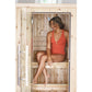 Model wearing coral red one-piece swimsuit sitting inside wooden sauna with glass door and wooden benches