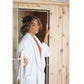 Model wearing white cardigan over coral top, standing in front of wooden sauna interior