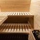 Interior view of wooden sauna with two bench levels, light pine construction, and rock heater basket in corner
