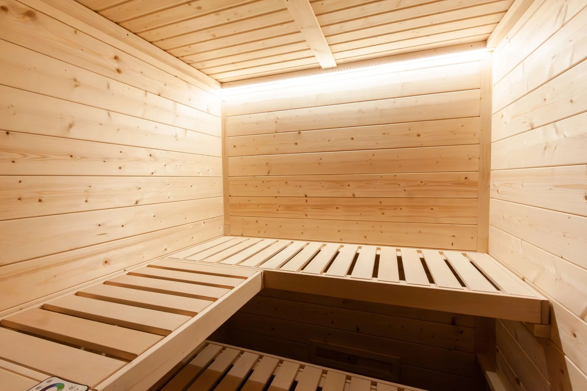 Interior view of natural wood sauna with two bench levels, horizontal wood paneling on walls and ceiling, and skylight openin