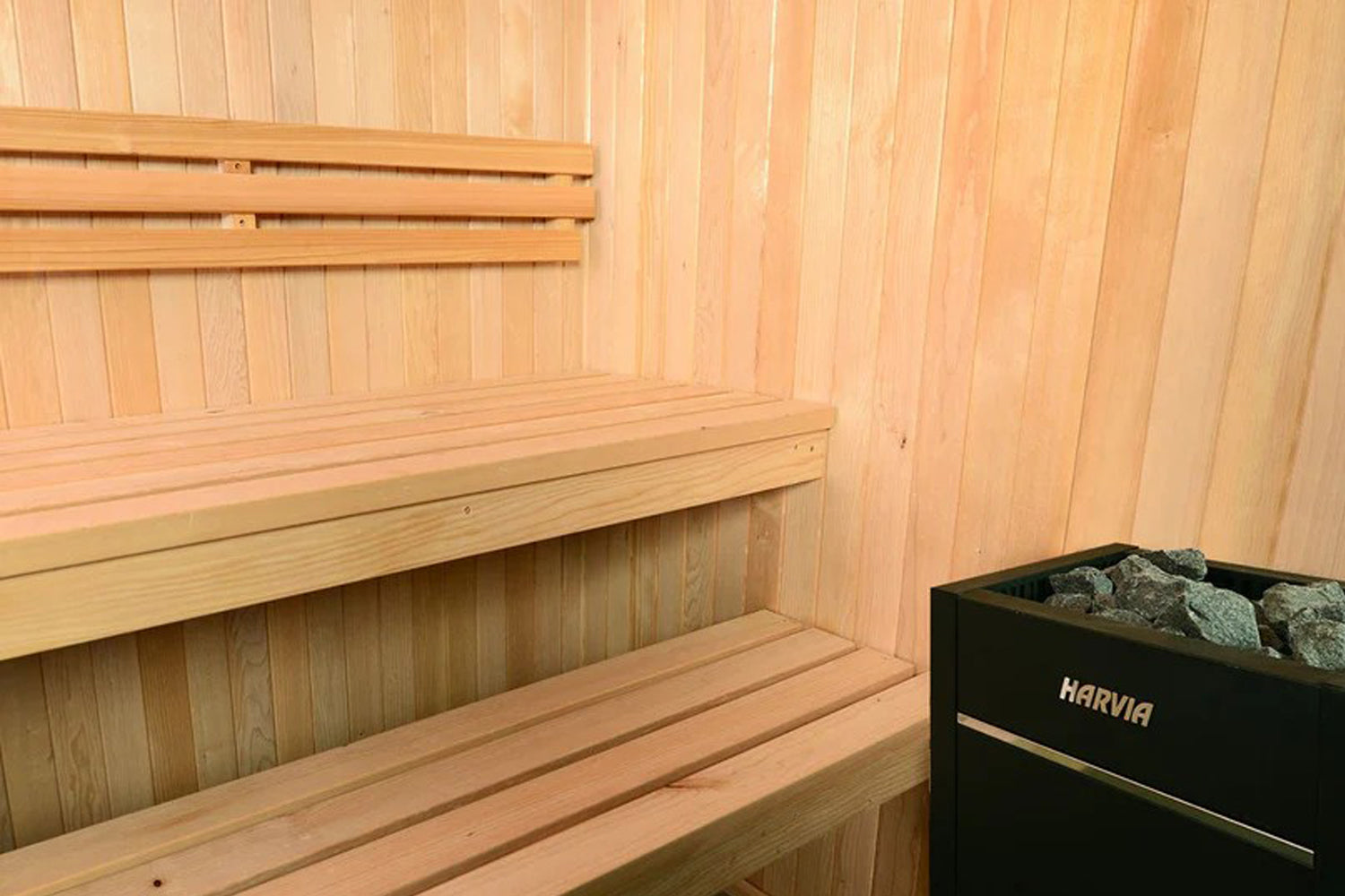 Almost Heaven Oasis 4-person indoor sauna with light wood interior, tiered benches, and black Harvia heater with stones visib