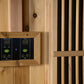 Wooden sauna control panel with digital temperature and timer displays, green power buttons, and adjustment controls mounted 