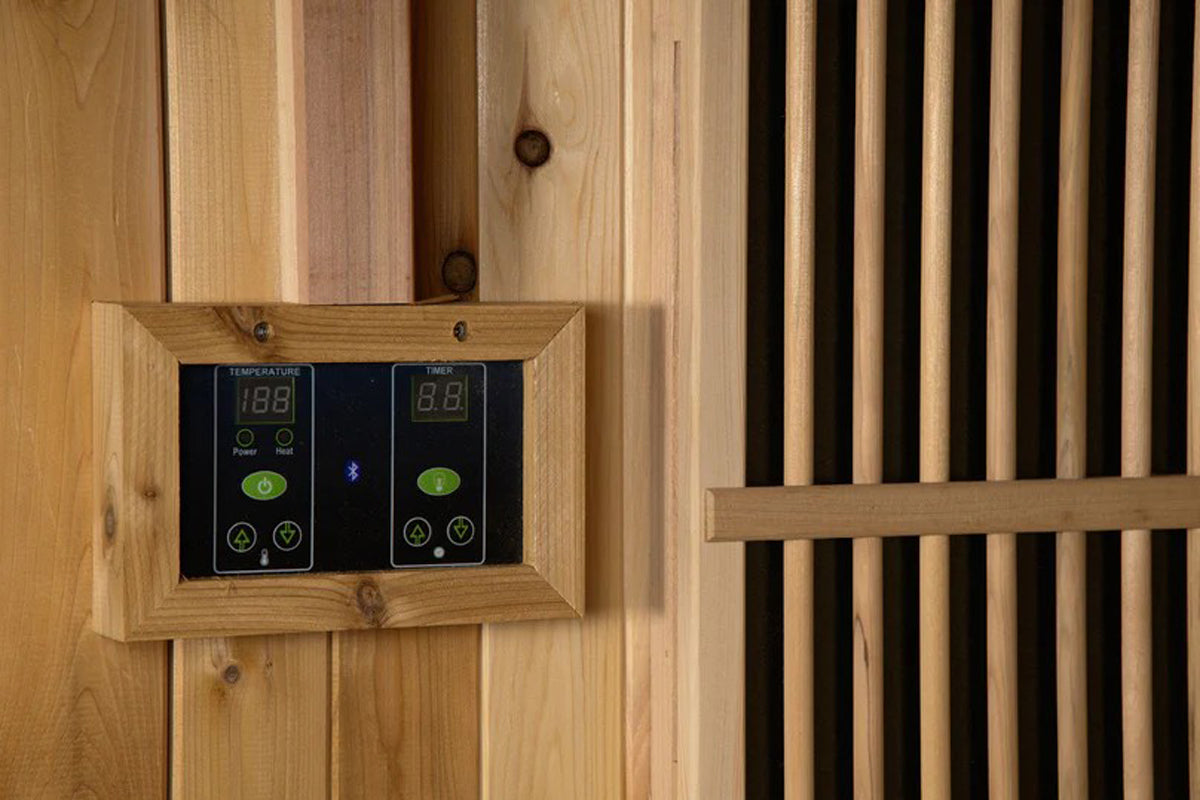 Wooden sauna control panel with digital temperature and timer displays, green power buttons, and adjustment controls mounted 