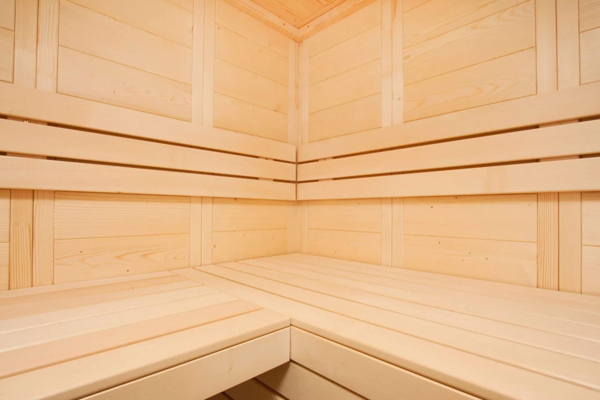 Interior view of wooden sauna with light pine benches and walls, corner seating arrangement