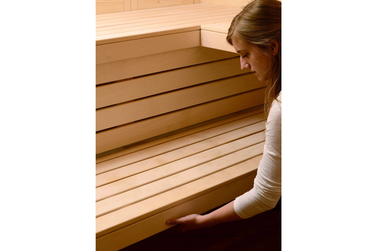 Woman in white long-sleeve shirt examining interior wooden benches of Almost Heaven Patterson corner sauna