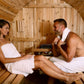 Couple sitting inside wooden barrel sauna wrapped in white towels, wooden interior visible
