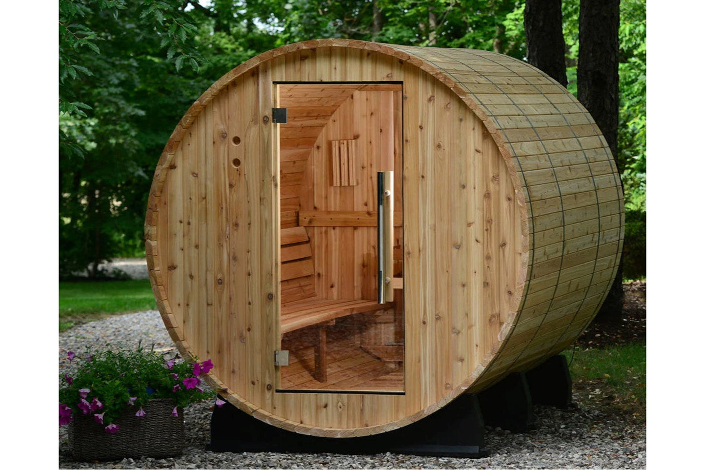 Cylindrical wooden barrel sauna with open door revealing cedar interior, benches, and ventilation, positioned in landscaped y